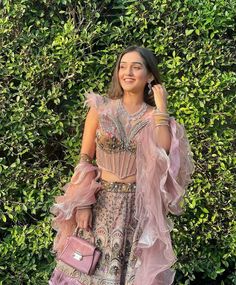 a woman standing in front of a bush holding a pink purse and talking on her cell phone