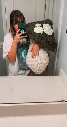 a woman taking a selfie in front of a mirror holding a cell phone and wearing a crocheted hat