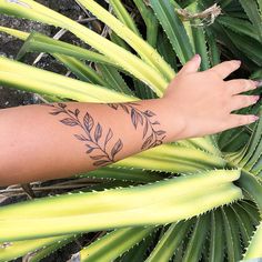 a person's arm with a tattoo on it next to some plants and leaves