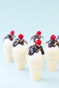 small ice cream cones with toppings on top are arranged in a row, against a light blue background