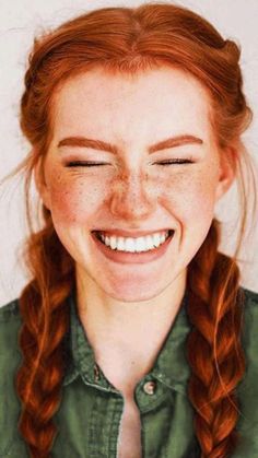 a woman with red hair and freckled eyes smiles at the camera while wearing a green shirt