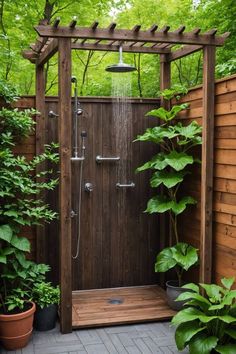 an outdoor shower in the middle of a garden with potted plants on either side