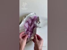 two hands are holding an object with purple fabric on it and silver foil around the edges