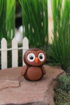 an owl figurine sitting on top of a rock next to some grass and bushes