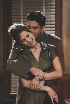 a man and woman hugging each other in front of a window with closed shutters