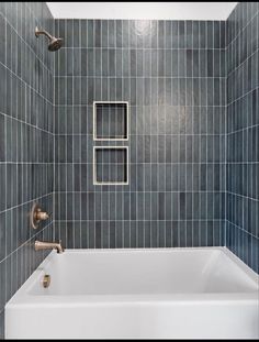 a bath tub sitting under a window next to a tiled shower head and hand held faucet