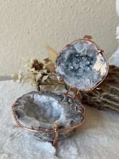 two pieces of metal sitting on top of a white table next to some dried flowers