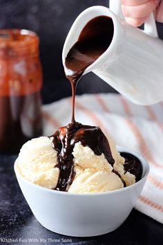 someone pouring chocolate sauce over ice cream in a white bowl on top of a table