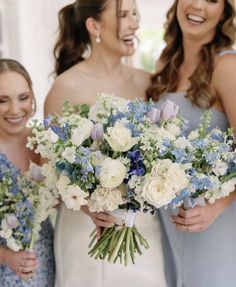 three bridesmaids holding bouquets of white and blue flowers smiling at each other