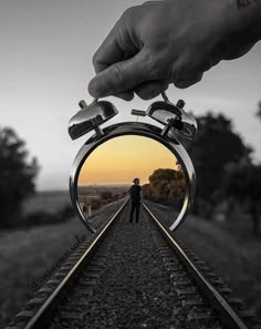 a person standing on train tracks with an alarm clock in front of them and the sun setting