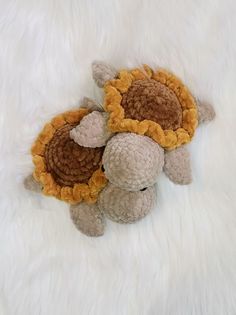 two crocheted stuffed animals laying on a white fur covered surface with one holding the other's head