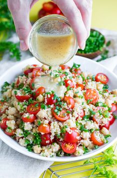 someone is pouring dressing into a bowl of food that includes tomatoes, chickpeas and couscous