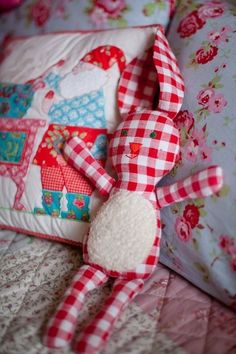 a red and white stuffed animal sitting on top of a bed next to pillow cases