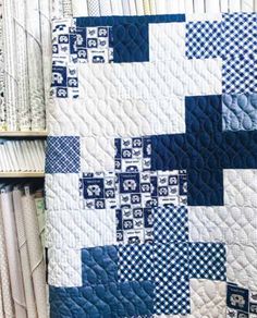 a blue and white quilt sitting on top of a book shelf next to stacks of books