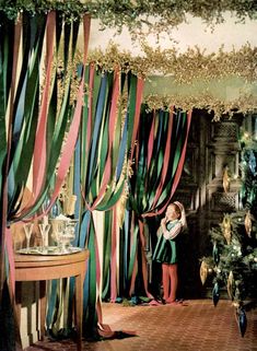 a child standing in front of a christmas tree with streamers hanging from it's ceiling