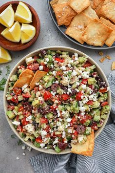 a bowl filled with salad next to crackers and lemon wedges on the side