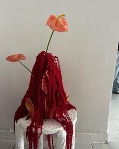 a white chair with red dreadlocks sitting on top of it next to a pink flower