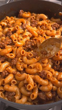 a skillet filled with macaroni and cheese being stirred with a wooden spoon