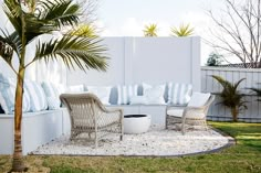 an outdoor seating area with palm trees and white walls in the back ground, surrounded by grass