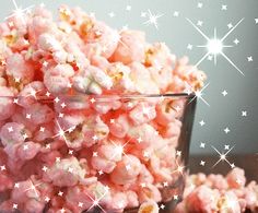 a glass bowl filled with pink popcorn on top of a wooden table covered in stars