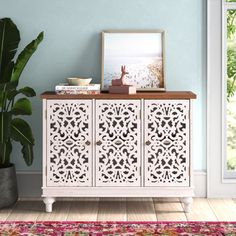 a white cabinet with carvings on the doors and drawers next to a potted plant