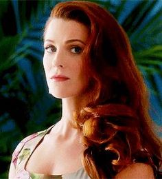 a woman with long red hair wearing a floral dress and looking off into the distance