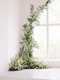 a window sill with flowers and greenery on it next to a white wall