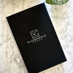 a black book sitting on top of a white counter next to a green cup and plant