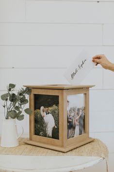 a wooden box with two photos in it on top of a table next to a potted plant