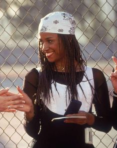 a woman with dreadlocks standing in front of a chain link fence giving the peace sign