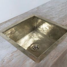 a square metal sink with a drain in the middle on a marble countertop top