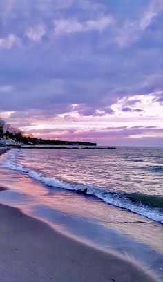 a beach with waves coming in to shore and the sun setting on the horizon behind it