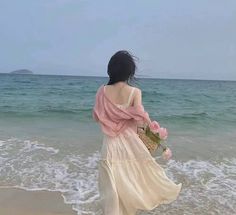 a woman standing on top of a beach next to the ocean holding a bouquet of flowers