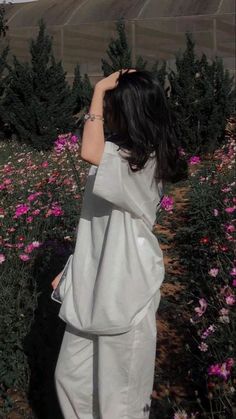 a woman standing in a field of flowers with her back to the camera, looking down