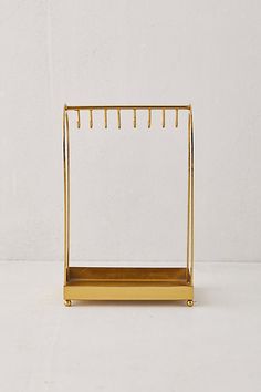 a golden metal rack with clothes hanging on it's sides and two hooks attached to the wall