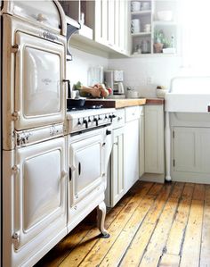 an old fashioned kitchen with white cabinets and wood flooring is seen in this image