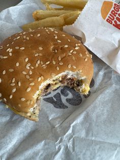 a burger and french fries sitting on top of a white paper wrapper next to each other