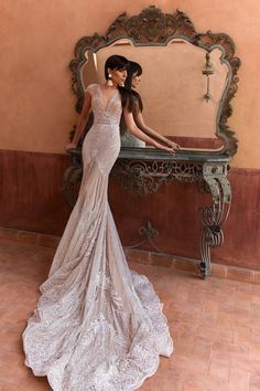 a woman standing in front of a mirror wearing a wedding dress with an open back