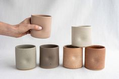 a hand is holding a coffee cup in front of five different sized cups on a white surface