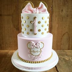 a pink and white cake with minnie mouse ears on it's top is decorated with gold polka dots