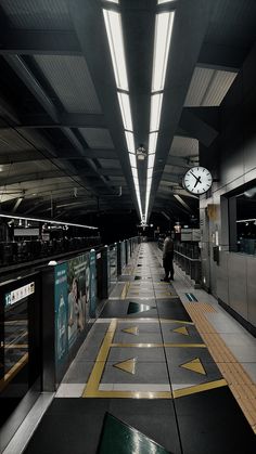 an empty train station with people walking on the platform and a clock hanging from the ceiling