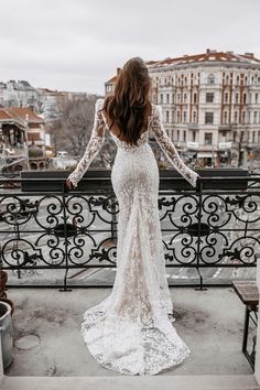 a woman standing on top of a balcony next to a railing wearing a white dress