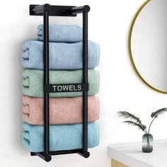 towels are stacked up on a towel rack in front of a mirror and potted plant