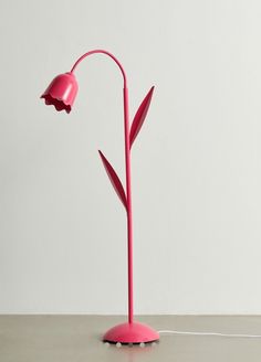 a pink floor lamp sitting on top of a table next to a white wall,