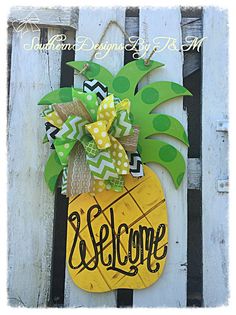 a pineapple door hanger with the word welcome on it and a green bow