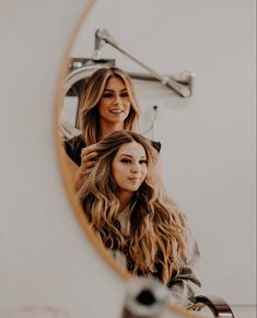 two beautiful young women sitting in front of a mirror looking at their hair and smiling