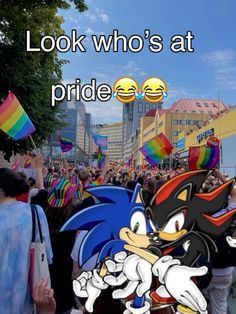 a crowd of people walking down a street next to tall buildings with rainbow flags in front of them