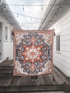 an orange and black rug is hanging on a string with lights strung above it in front of a white house