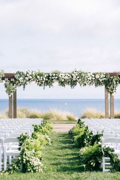 an outdoor ceremony set up with white chairs and greenery on the grass, overlooking the ocean