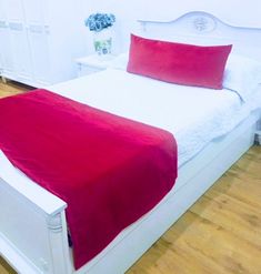 a white bed with red sheets and pillows in a room that has wood floors, cabinets, and hardwood flooring